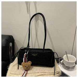 Detail of black minimalist shoulder bag with teddy bear pendant on beige knit