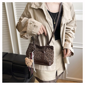 Detail view of leopard print crossbody bag with cute plush bear charm and leather strap