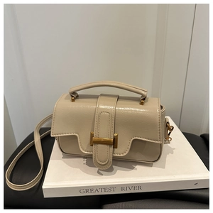 Détail d'un sac crème avec texture cuir et boucle en métal doré posé sur un livre