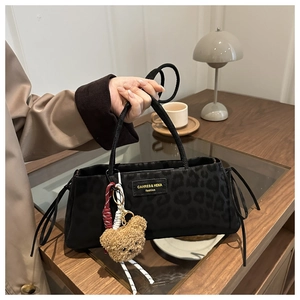 Detail of black leopard print shoulder bag with plush bear charm and woven cord