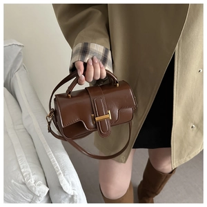 Détail du sac bandoulière en cuir marron foncé avec boucle dorée sur un trench-coat élégant