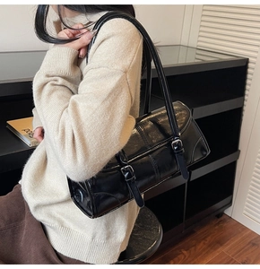 Side view of a glossy black patent leather underarm bag with silver buckles on a model