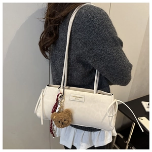 Detailed side view of off-white rectangle shoulder bag with teddy bear charm and twin straps