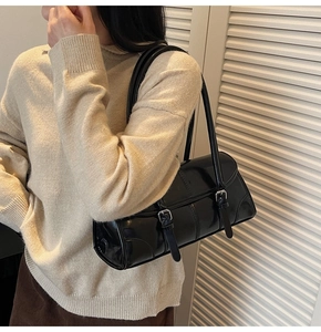 Detailed view of black glossy shoulder bag with dual silver buckles worn by a model