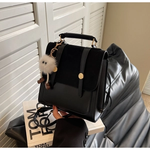 Detail of black leather mixed-texture backpack with golden buckle and fluffy monster charm