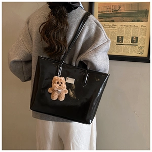 Detail shot of black glossy patent leather shoulder bag with a cute brown plush bear charm