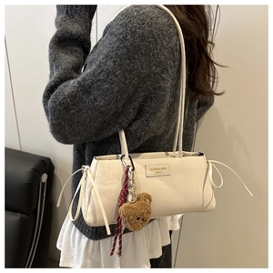 Detailed side view of white faux leather shoulder bag with bow ties and bear charm