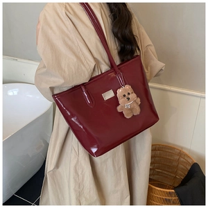 Burgundy patent leather tote bag detail with glossy finish and plush bear charm