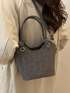 Chic grey leopard print bucket bag with dual handles and gold hardware worn with beige coat