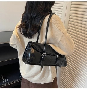 Detail of black glossy leather underarm bag with double buckle straps and long shoulder strap