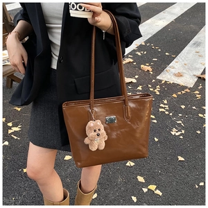 Detail of dark brown glossy shoulder bag with plush dog charm and silver logo plate