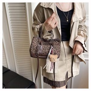 Detail of leopard print bucket bag with leather handles and cute plush bear charm