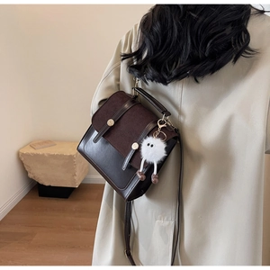 Detail of dark brown vintage crossbody bag with metal buckles and plush monster charm