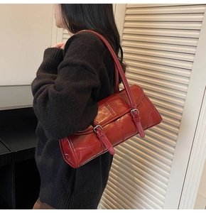 Detail view of a dark red patent leather baguette bag with buckles shown on a model shoulder