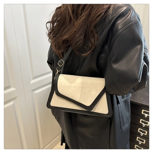 Side view of a beige and black contrast crossbody bag with gold hardware worn by a model