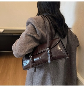 Close-up of deep chocolate glossy leather underarm bag worn by a model in a warm setting