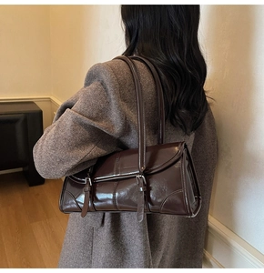 Detail view of dark brown glossy baguette bag with metal buckles on grey wool coat
