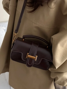 Sac bandoulière rétro en cuir marron foncé avec boucles dorées porté avec un trench