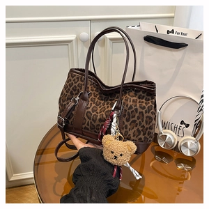 Detail of leopard print tote bag featuring brown leather straps and a plush bear charm