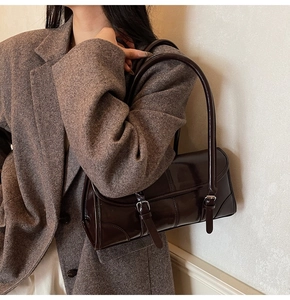 Detail of dark brown glossy leather baguette bag with dual buckles on wool blazer
