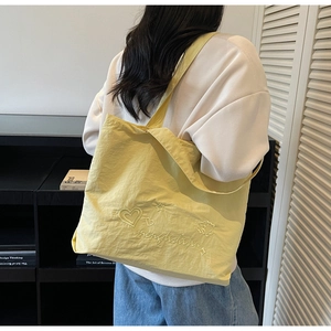 Detail of yellow tote bag with embroidered heart and star patterns on nylon fabric