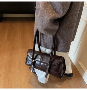 Detail of dark chocolate glossy leather shoulder bag with vintage buckle straps and long handles