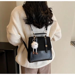 Detail of black matte leather backpack with flap closure, metal buckle and white fur charm