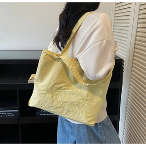 Detail of yellow nylon tote bag with embroidered letters and stars on shoulder