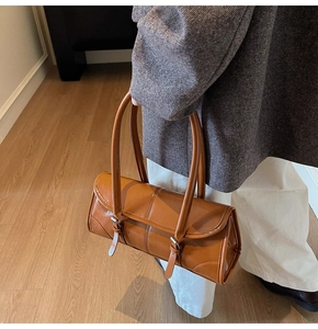 Detail of caramel leather baguette bag with dual decorative buckle straps on model