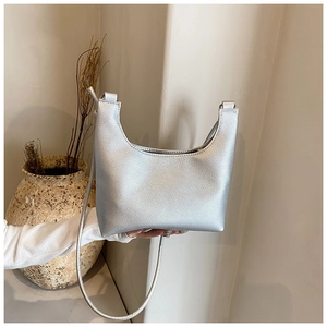 Detailed view of a silver textured leather shoulder bag held by a hand in a minimalist setting