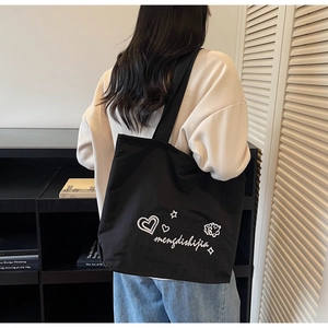 Detail of black canvas tote bag featuring white hand-drawn heart and star graphics