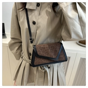 Close-up of leopard print envelope crossbody bag with black trim and thin strap on a model