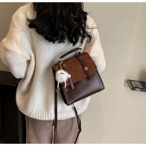 Detail of dark brown leather and suede backpack with golden buckles and plush monster charm