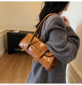 Detail view of tan glossy leather underarm bag with decorative metal buckles