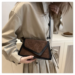 Close-up of a stylish leopard print flap crossbody bag worn with a beige trench coat