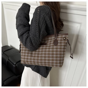 Detail of plaid tote bag showing textured wool fabric and brown leather trim accents