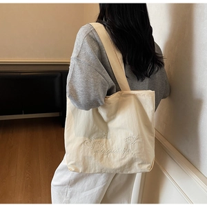 Detail of off-white canvas tote bag featuring delicate embroidery and wide shoulder strap