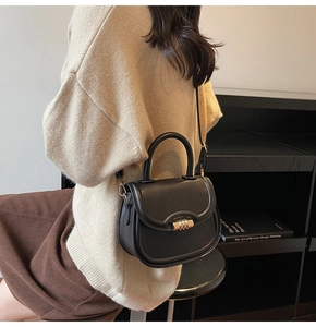 Detail of a black leather saddle bag featuring a cylinder gold lock and versatile strap