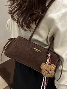 Leopard print underarm bag with plush bear charm and side tassel accents