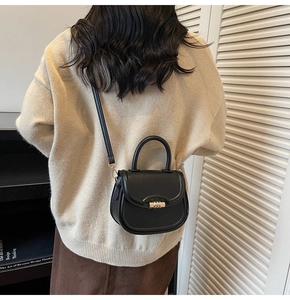 Detail of a black leather saddle bag with gold metal hardware worn with a beige sweater