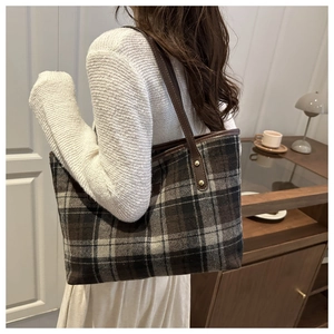 Detail of vintage plaid tote bag with brown leather strap worn by a model in a cozy cafe