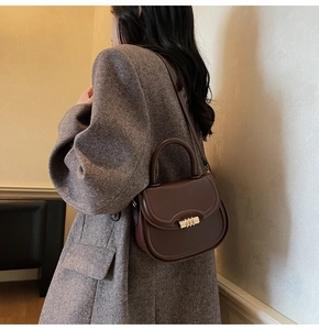 Detail of dark brown leather saddle bag with gold metal buckle on grey tweed coat