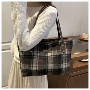 Detail of checkered tote bag featuring woven wool fabric and brown leather trim with rivets
