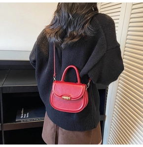 Model view of a red leather saddle bag with a golden clasp and shoulder strap details