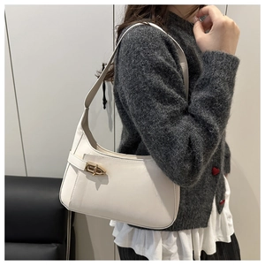 Side view of model wearing a minimalist beige crescent underarm bag with gold metal clasp