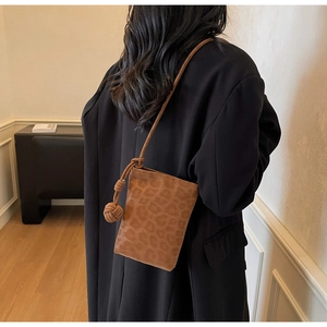 Detail of leopard print crossbody bag with woven ball knot on shoulder strap