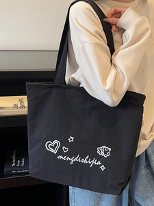 Minimalist black canvas tote bag with white embroidery shown on shoulder