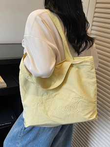 Minimalist light yellow embroidered tote bag shown worn by a model in a lifestyle setting