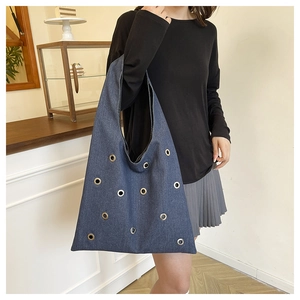 Détail du sac cabas en jean bleu marine avec œillets métalliques porté par un mannequin