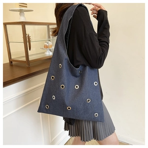 Détail du sac cabas en denim bleu foncé avec de grandes décorations d'œillets métalliques